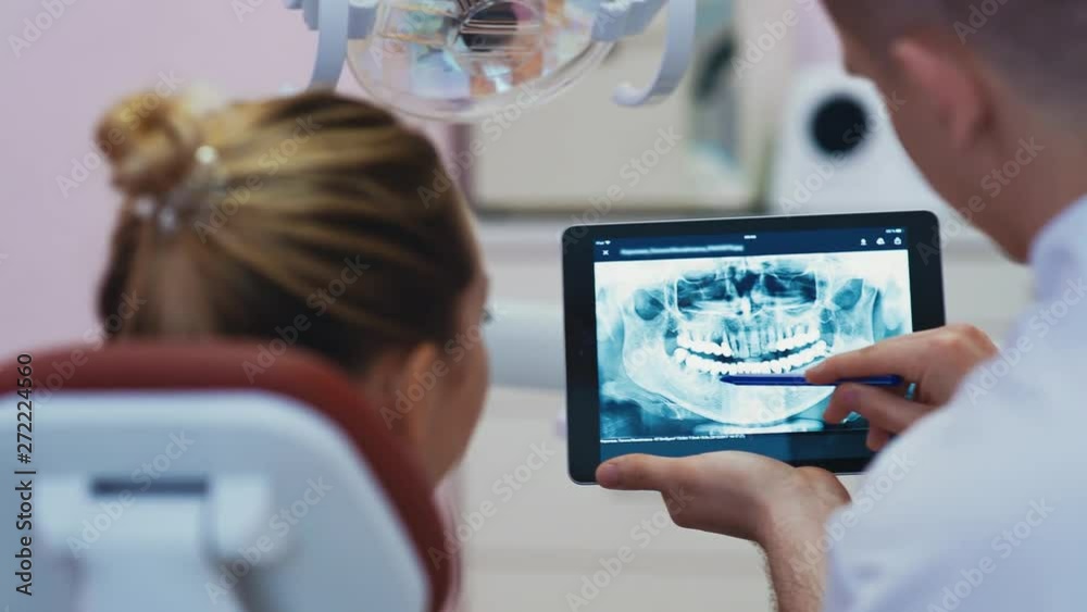 Dentist showing teeth xray on tablet sitting before dental chair in