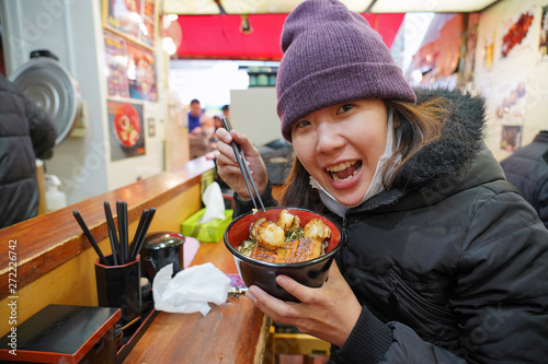 Asian young woman enjoy with japanese food which have rice with eel griled and scallop in the bowl in fish market, tokyo, japan photo