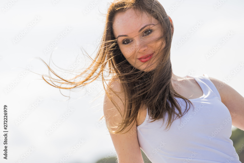 Gorgeous romantic girl outdoors. Brown long hair blowing in the wind against sky.