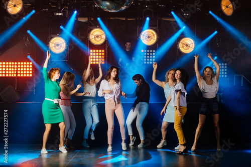 Group of eight energetic girls friends dancing in night club. Full height portrait. Light rays on background. Party, holidays, celebration, nightlife and people concept.