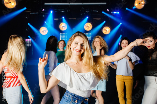 Pretty female women clubber dancing surrounded by her friends and looking at camera with smile during holidays party relaxing celebrating dancing at party in night club together.
