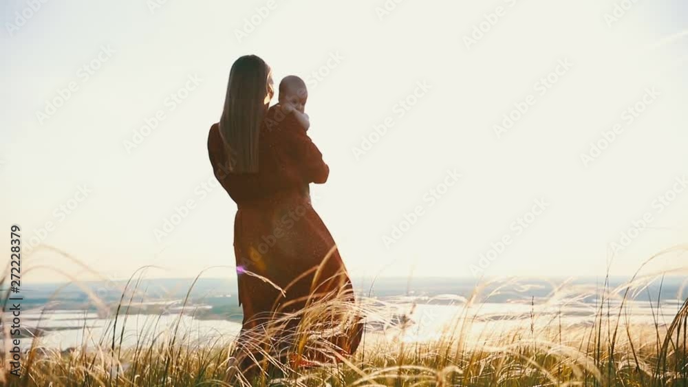 A woman holds a child in her arms. Against the backdrop of the sunset.