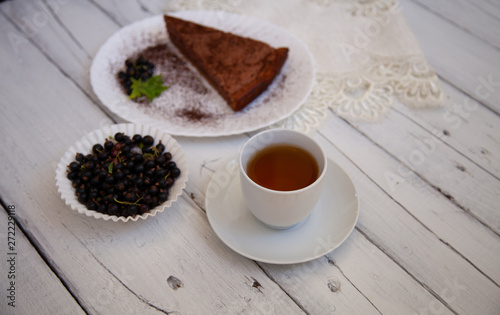 chocolate cake slice with a white cup of tea and a handful of currants