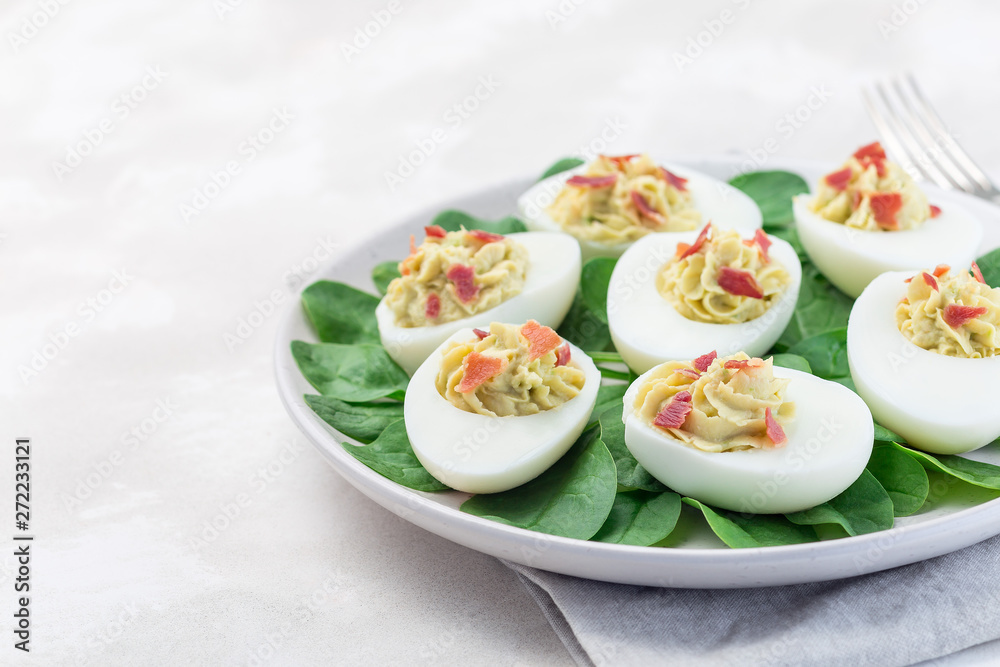 Deviled eggs stuffed with avocado, egg yolk and mayonnaise filling, garnished with bacon on spinach leaves, horizontal copy space Deviled eggs stuffed with avocado, egg yolk and mayonnaise filling, garnished with bacon on spinach leaves, horizontal copy space