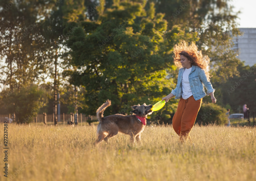 Young beautiful curly girl playing with her dog with a frisbee in summer park Young beautiful curly girl playing with her dog with a frisbee in summer park