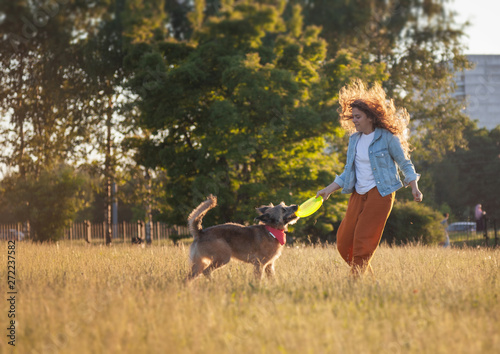 Young beautiful curly girl playing with her dog with a  frisbee in summer park