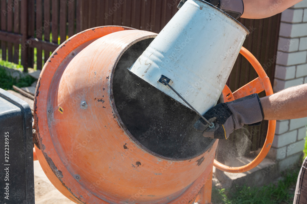 builder working with shovel during concrete cement solution mortar preparation. construction worker with a bucket in his hands loads a concrete mixer.orange concrete mixer prepares cement mortar