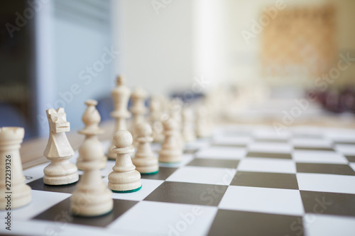Black and white chess board with white wooden figures on table with blurred background