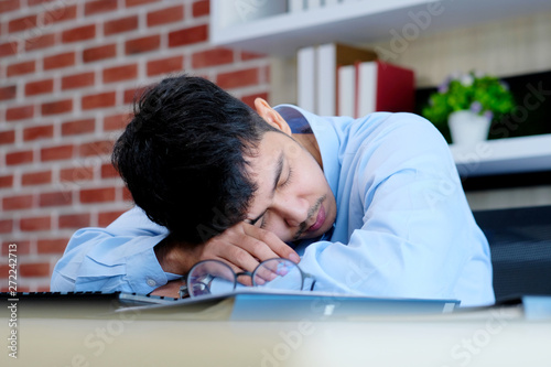 Tired asian man sleeping at office desk. Young businessman with eyeglasses overworked and fell asleep, Creative casual man sleeping at his working place