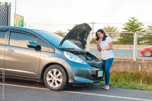 Asian teenage women holding a mobile phone Walking around the car, stressful mood during the evening hours. Along the highway Because her car broke down And she is waiting for help from someone. © BNMK0819