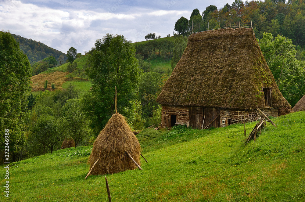 Romanian hovel with thatch and straw bundle near, in beautiful wild country. Romanian rurality with typical building with straw roof. Romanian hovel with thatch and straw bundle near, in beautiful wild country. Romanian rurality with typical building with straw roof.