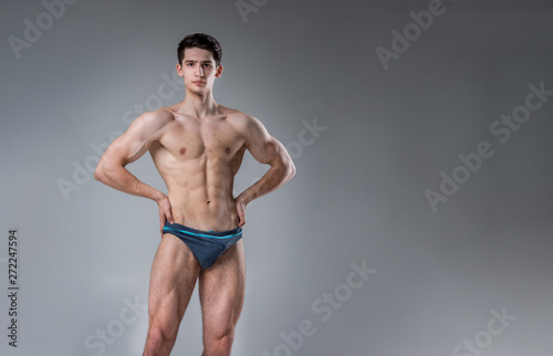 Young male athlete bodybuilder posing. Handsome athletic male power guy. Fitness muscular person. Young athlete showing muscles in the studio. six packs muscles posing shirtless on gray background