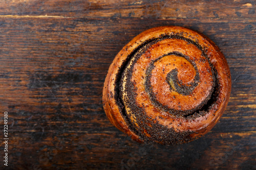 Sweet homemade bun with poppy seeds on a wooden background