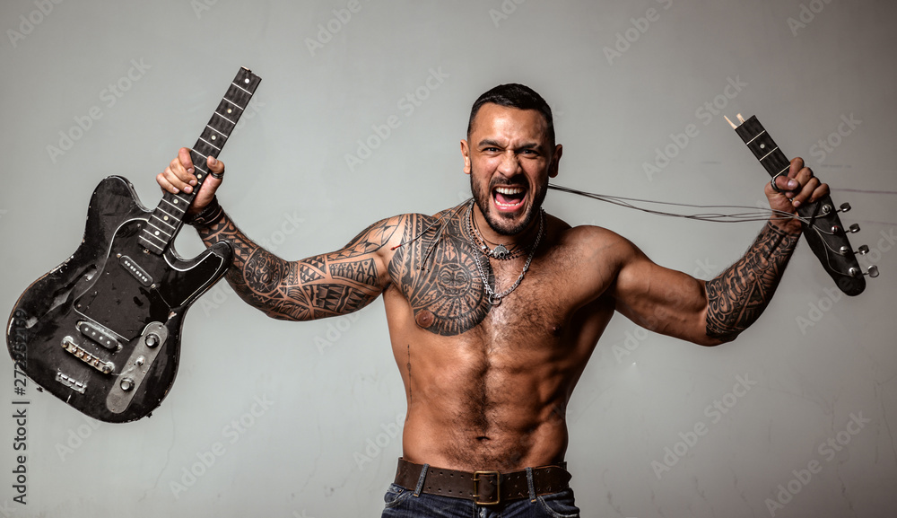 Foto de Music shop. Dj excited. Stylish brutal man with a beard, a tattoo  is shattering electric guitar. Sexy look of a male model. Advertising music  shop concept. Copy space. do Stock