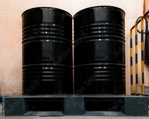 Low light inside of factory. Two black tanks chemical packaging with old and stained.