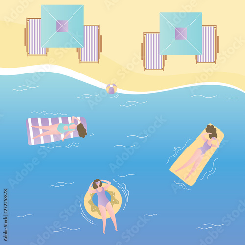 Girls on inflatable mattresses swim in sea,umbrellas and deck chairs on the beach