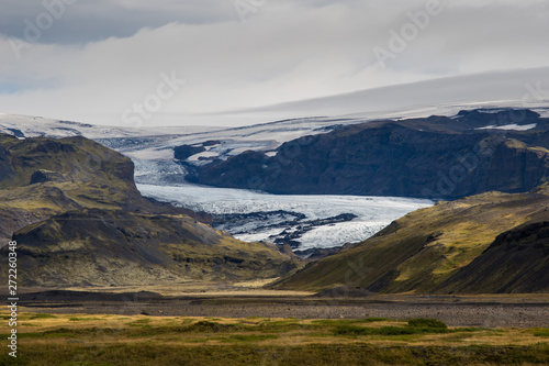 Tongue of Glacier Eyjafjallajökull in Iceland drifting down from the green moss mountain in the foggy day. Blue glacier ice is visible, as well as green moss covering rocks of the mountain