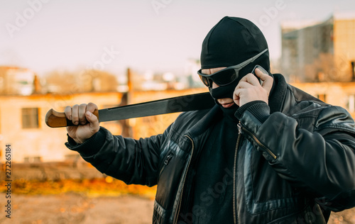 bandit with a machete in a black mask talking on the phone