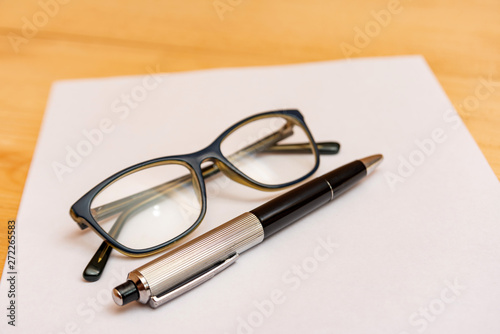 Eyeglasses and a pen lie on a clean and white sheet of paper for recording.