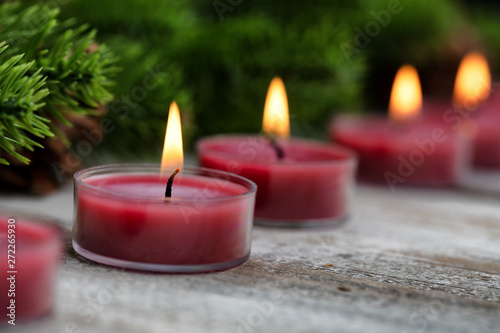 Close up view of traditional glowing Christmas holiday candles with evergreen in background