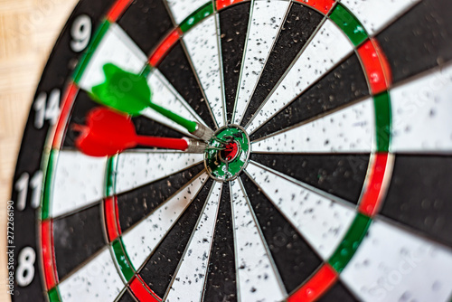 A round board for playing darts close up, red and green darts hit the target.