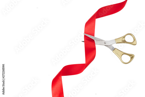 Grand opening. Top view of gold scissors cutting red ribbon on wite background.