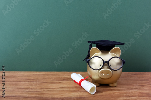 Gfold piggy bank with a grad cap and diploma in front of green chalkboard. Education scholarship photo