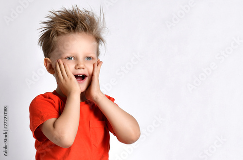 Happy smiling kid boy in orange t-shirt with his hands on his face looks at something amazing on white