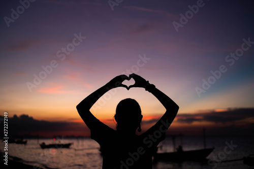 Woman making heart symbol with hands at sunset.