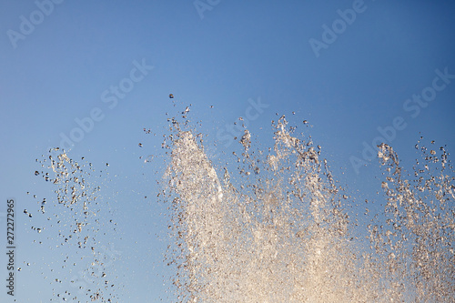 Close-up on splashes from the streams of an artificial fountain from which water flows in drops in the city park against the blue sky on a warm summer sunny day