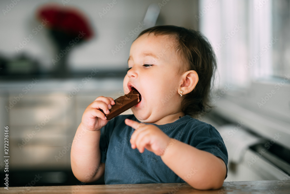 little girl in the afternoon in the kitchen eating a delicious chocolate bar little girl in the afternoon in the kitchen eating a delicious chocolate bar