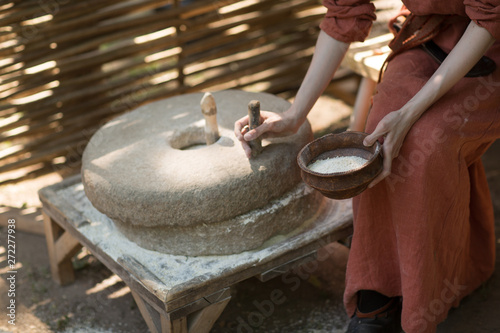 Fototapeta Woman grinds wheat and makes flour on millstone