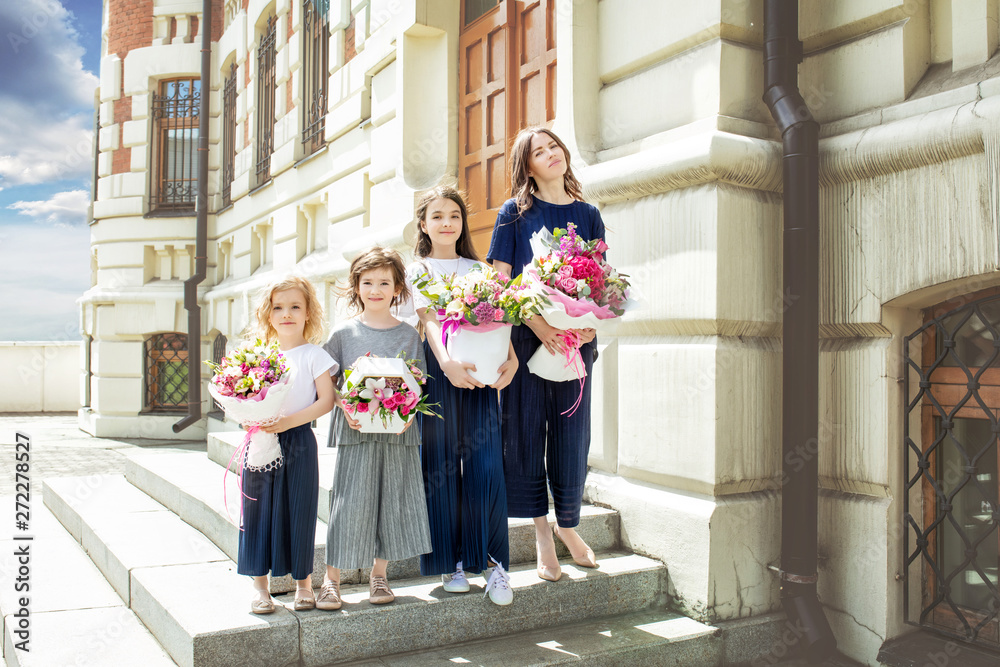 Young beautiful adult mother and her little cheerful and happy daughters with bouquets of flowers on the background of city streets