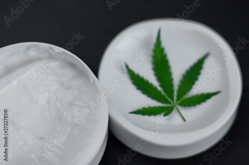 Close up of jar of cream from biological and ecological plants of hemp vegetable pharmaceutical oil CBD with green cannabis leaf with copy space