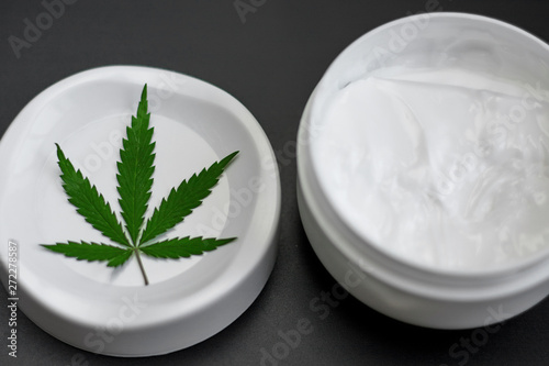 Close up of jar of cream from biological and ecological plants of hemp vegetable pharmaceutical oil CBD with green cannabis leaf with copy space
