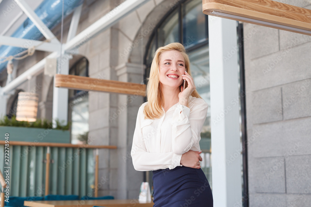 Charming young woman in formal suit talking on smartphone during lunch break in large spacious office in business center Charming young woman in formal suit talking on smartphone during lunch break in large spacious office in business center