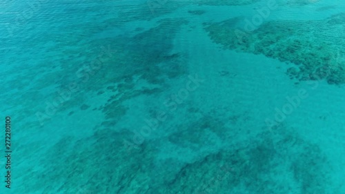 Slowly flying over clear blue water with the bottom visible through. photo