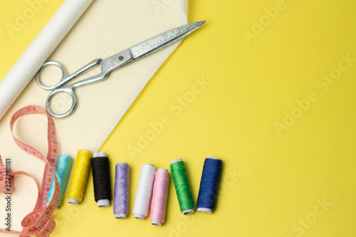 Sewing accessories and fabric on a yelow background. Sewing threads, pins, pattern and sewing centimeter. For sewing at home.Top view, flatlay