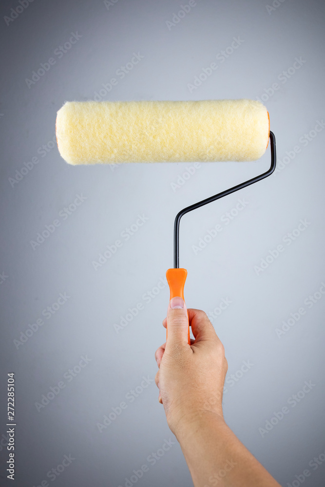 Obraz premium Man holding paint roller on gray background.