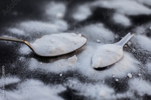 Raw powdered baking soda in a antique spoon on wooden surface along with some more in a plastic spoon.Horizontal shot. photo