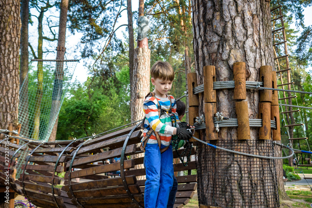 boy having fun at adventure park. toddler climbing in a rope playground structure. toddler climbing in a rope playground structure. Safe Climbing extreme sport with helmet and Carabiner