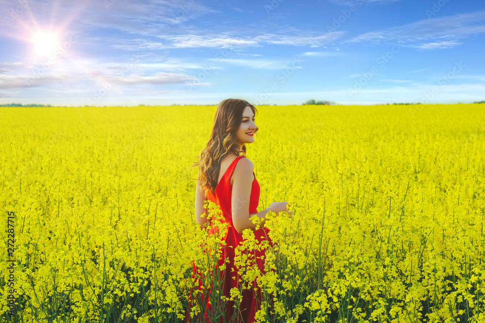Young beautiful girl in a red dress close up in the middle of yellow field with radish flowers and sunlight.. Young beautiful girl in a red dress close up in the middle of yellow field with radish flowers and sunlight..