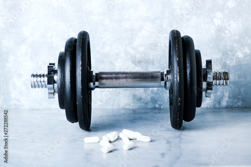 Black heavy dumbbell and creatine capsules on rustic background. Fitness or bodybuilding background  Copy space. 