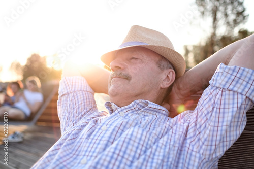 Old hispanic man sits on bench, smiling, enjoying summer sunny day. All problems left behind. Concept of happy retired person