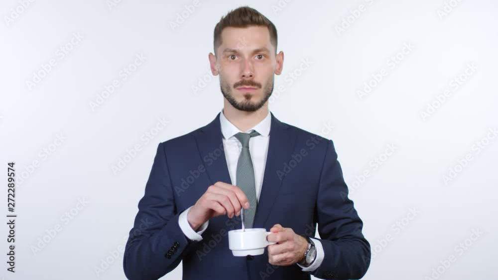 Cinemagraph of emotionless businessman in suit and necktie standing isolated on white background and stirring tea or coffee in cup while staring at cameraCinemagraph of emotionless businessman in suit Cinemagraph of emotionless businessman in suit and necktie standing isolated on white background and stirring tea or coffee in cup while staring at cameraCinemagraph of emotionless businessman in suit