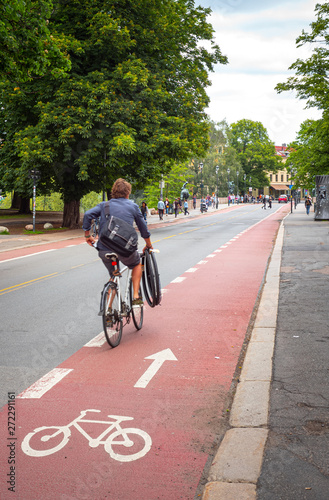 Man cycling along a marked bicycle lane, holding extra extra bicycle tires © ajwk