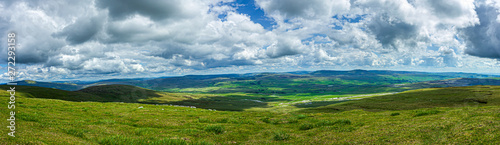 A panoramic view of a mountain valley with grassy green slope under a majestic blue sky and white clouds