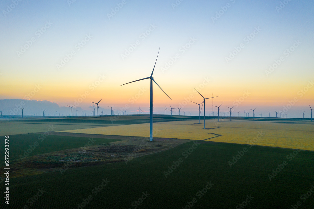 Aerial view of Eolian generators in a beautiful wheat field. Eolian turbine farm. Wind turbine silhouette. Wind field turbines. Wind propeller. Electric power production. Green energy. Morning light Aerial view of Eolian generators in a beautiful wheat field. Eolian turbine farm. Wind turbine silhouette. Wind field turbines. Wind propeller. Electric power production. Green energy. Morning light