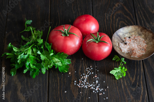 Fresh tomatoes with parsley and salt on a dark wooden background. Copy space. Harvesting tomatoes. 