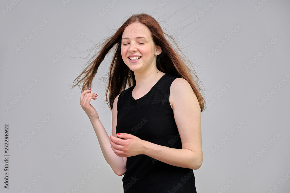 Photo portrait of a beautiful young pretty girl with dark red hair on a gray background in a black jacket. It stands directly in front of the camera in various poses, smiling, happy with life. Photo portrait of a beautiful young pretty girl with dark red hair on a gray background in a black jacket. It stands directly in front of the camera in various poses, smiling, happy with life.